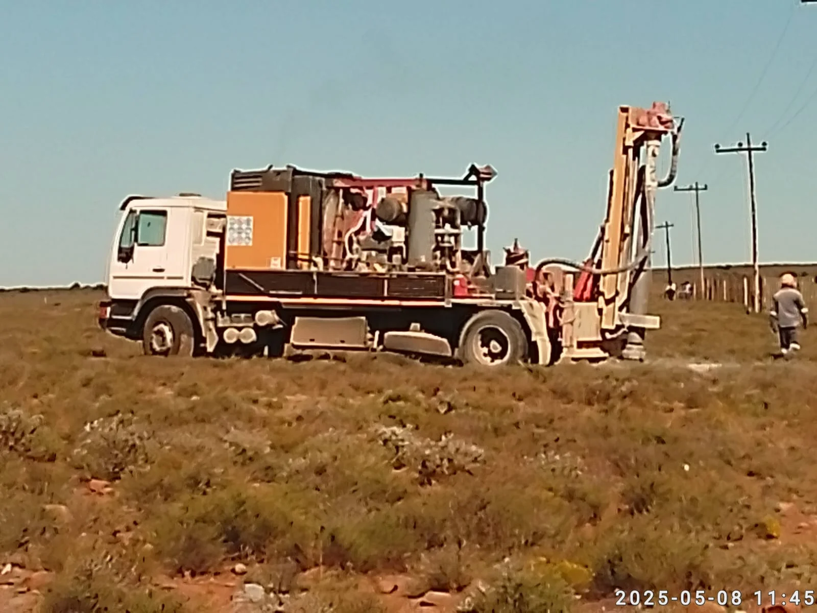Overhead electricity distribution fieldwork with drilling rig and distribution line route